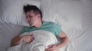 年轻的男人。睡眠噩梦坏梦想担心白色床上用品绿松石蓝色的t恤黑暗头发前视图